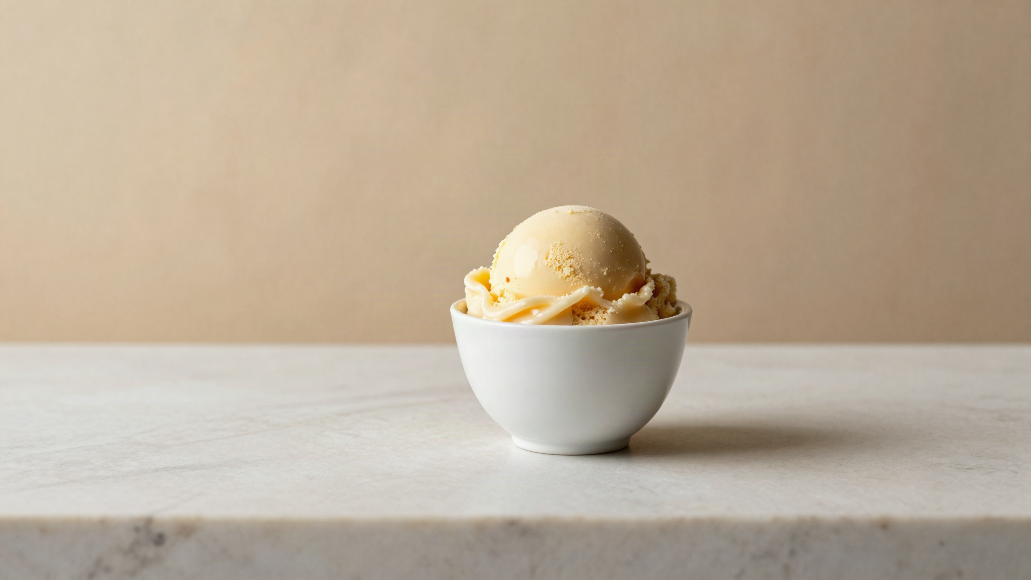 Pale caramel toasted milk gelato served in a small white ceramic cup on marble