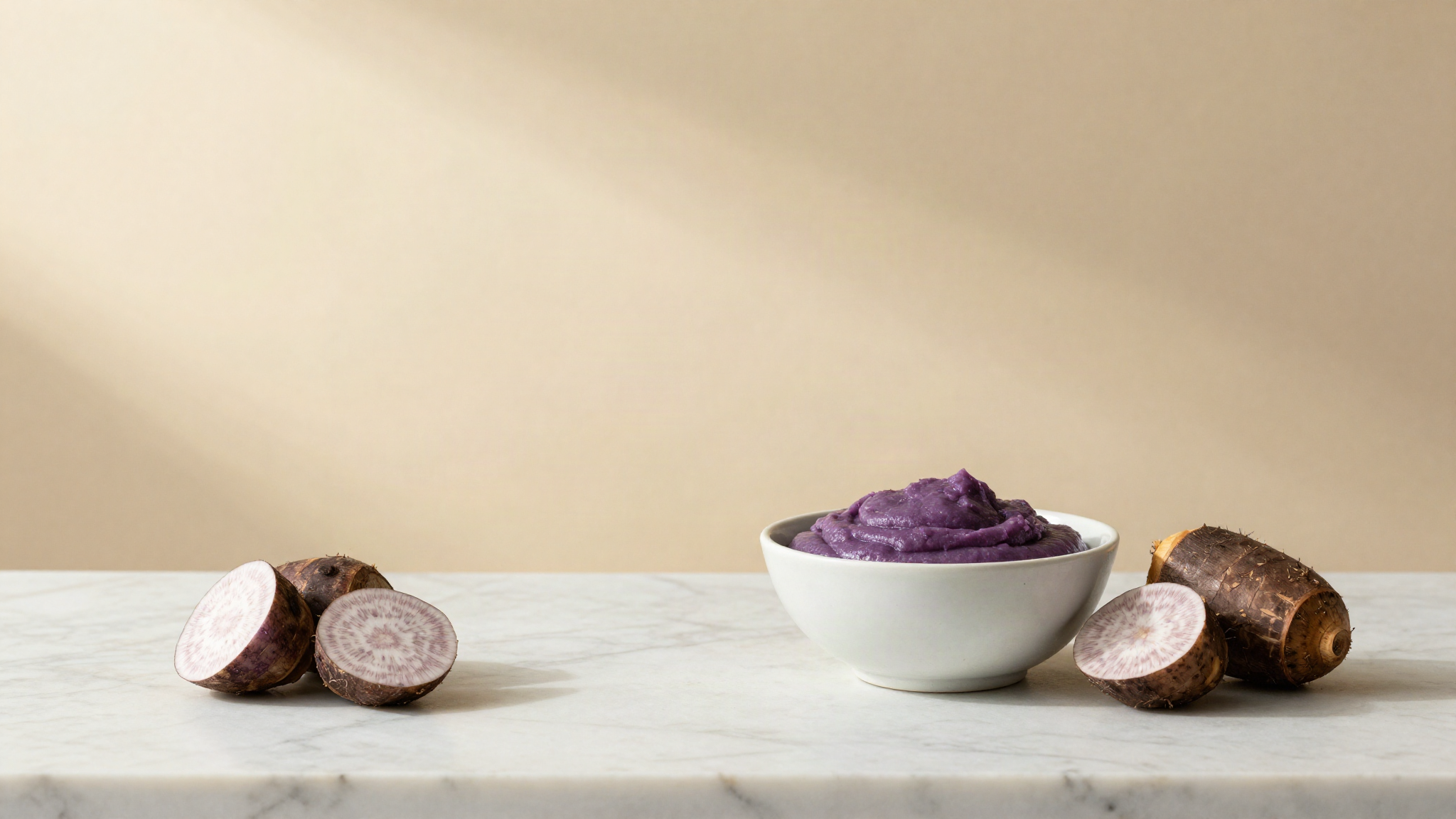 A bowl of smooth cooked purple yam paste beside pieces of steamed purple tuber