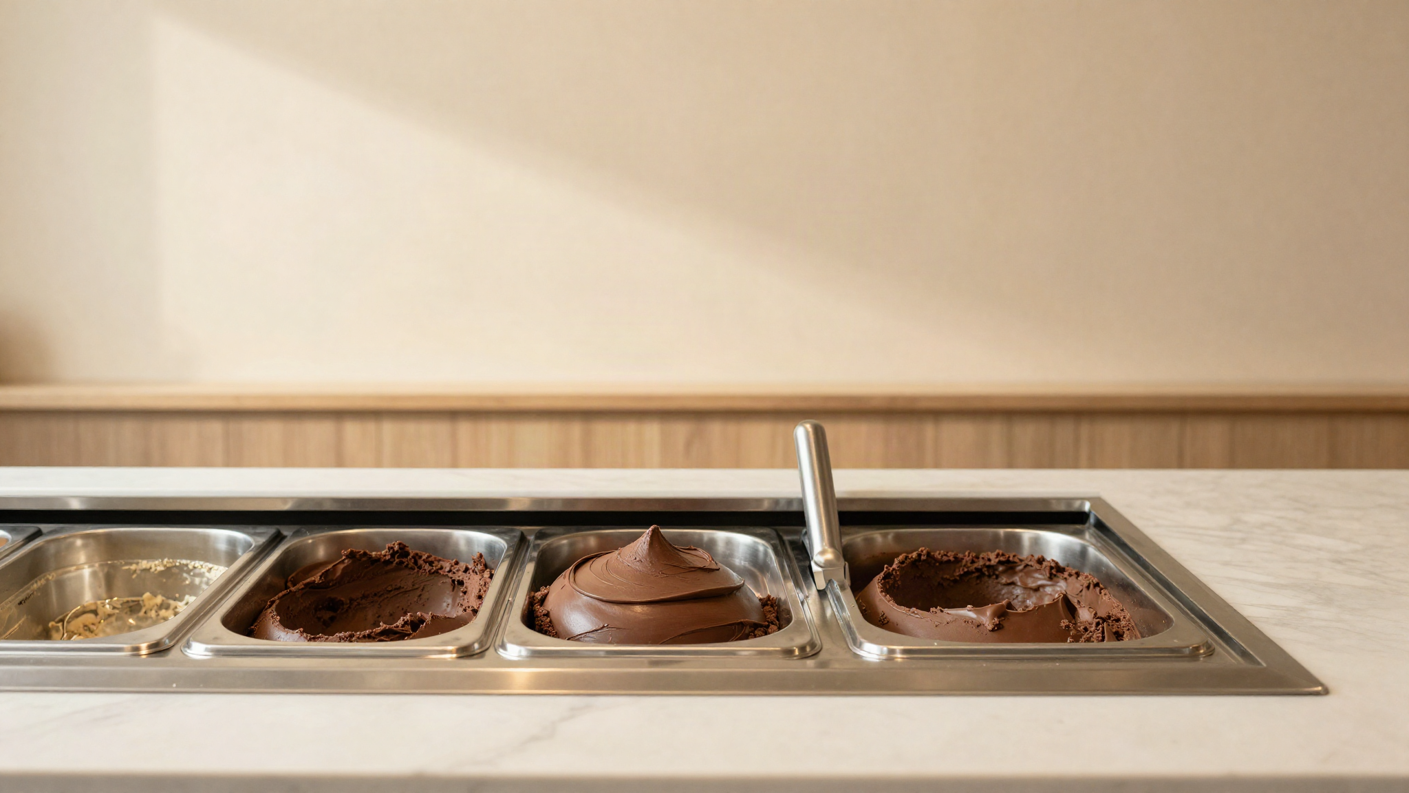 A gelato display pan of dark chocolate gelato with a smooth scooped surface in a clean gelateria counter, soft natural light