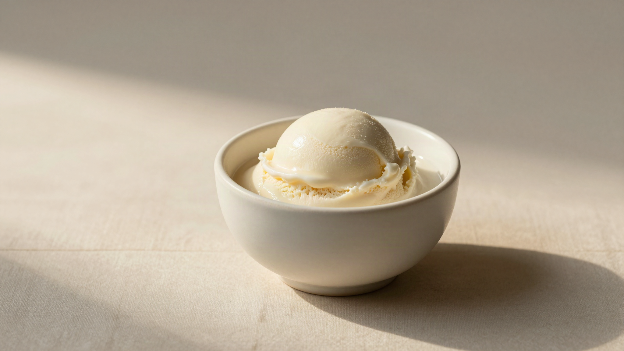 A pale ivory scoop of neutral vegan gelato base in a small white ceramic cup on light marble