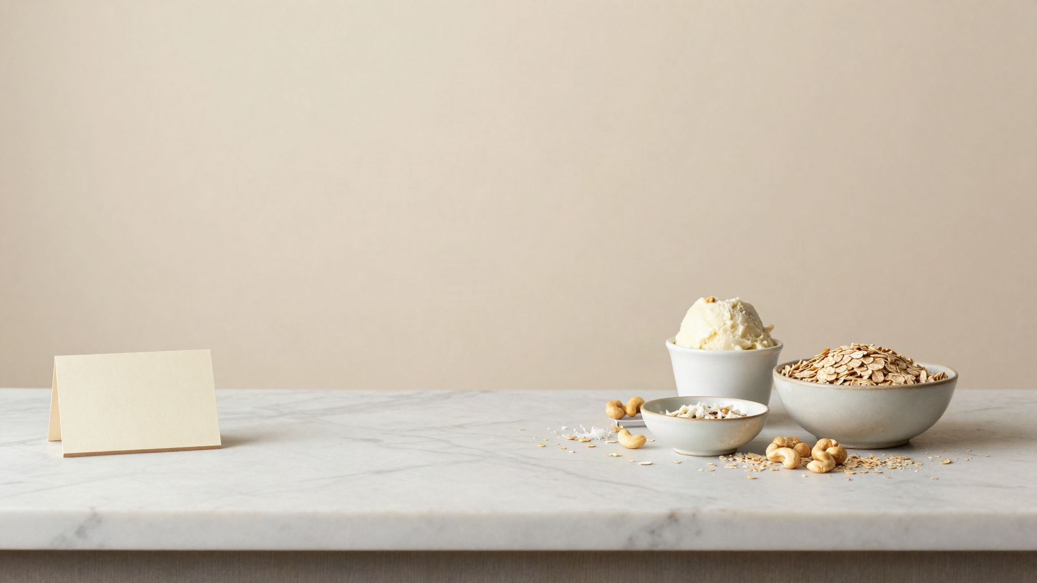 A blank tub label beside a cup of plant based gelato and small dishes of oats, cashews and coconut on a marble counter