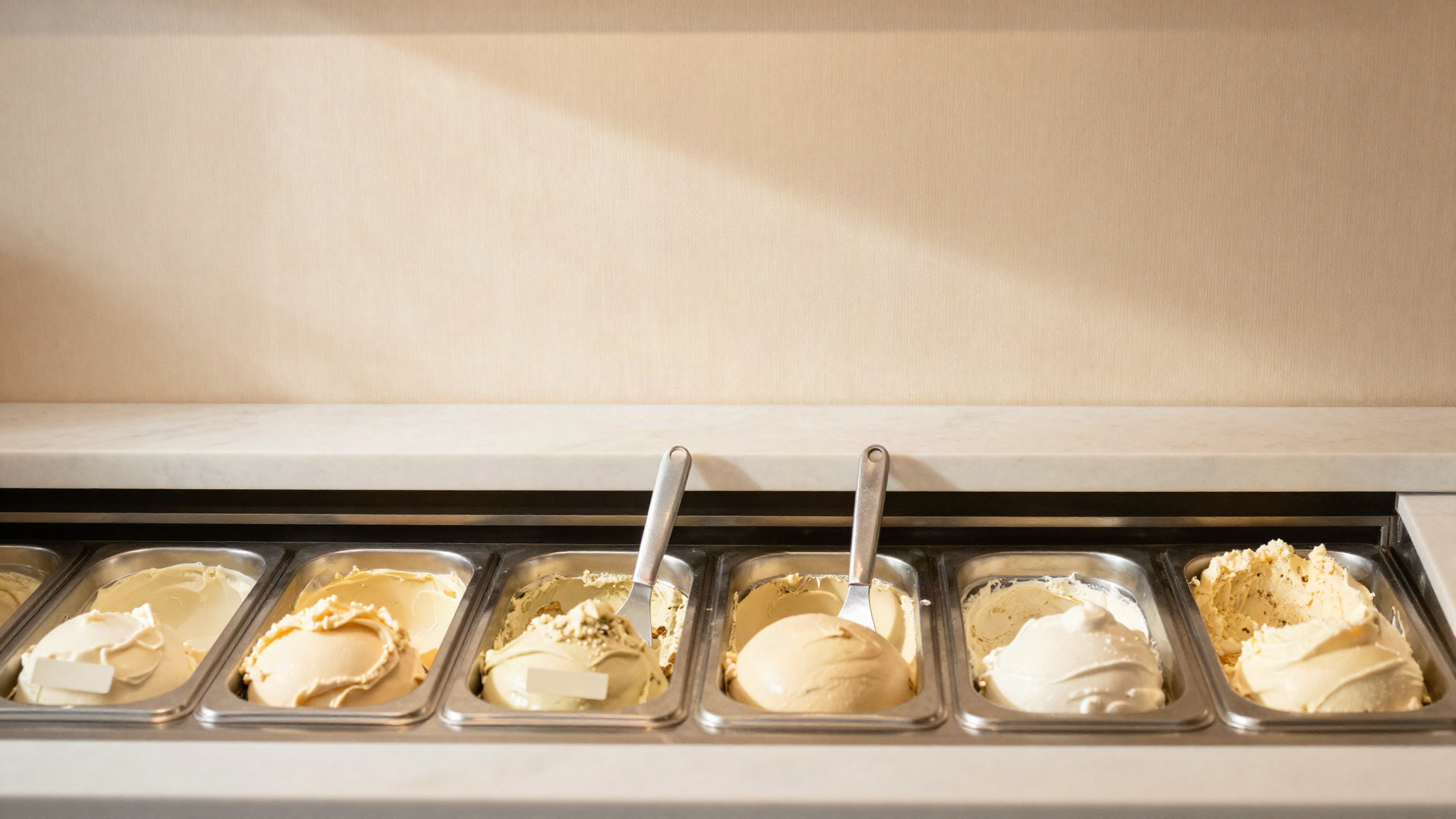 A tidy gelato cabinet with plant based tubs grouped at one end and a separate clean spatula standing in each tub