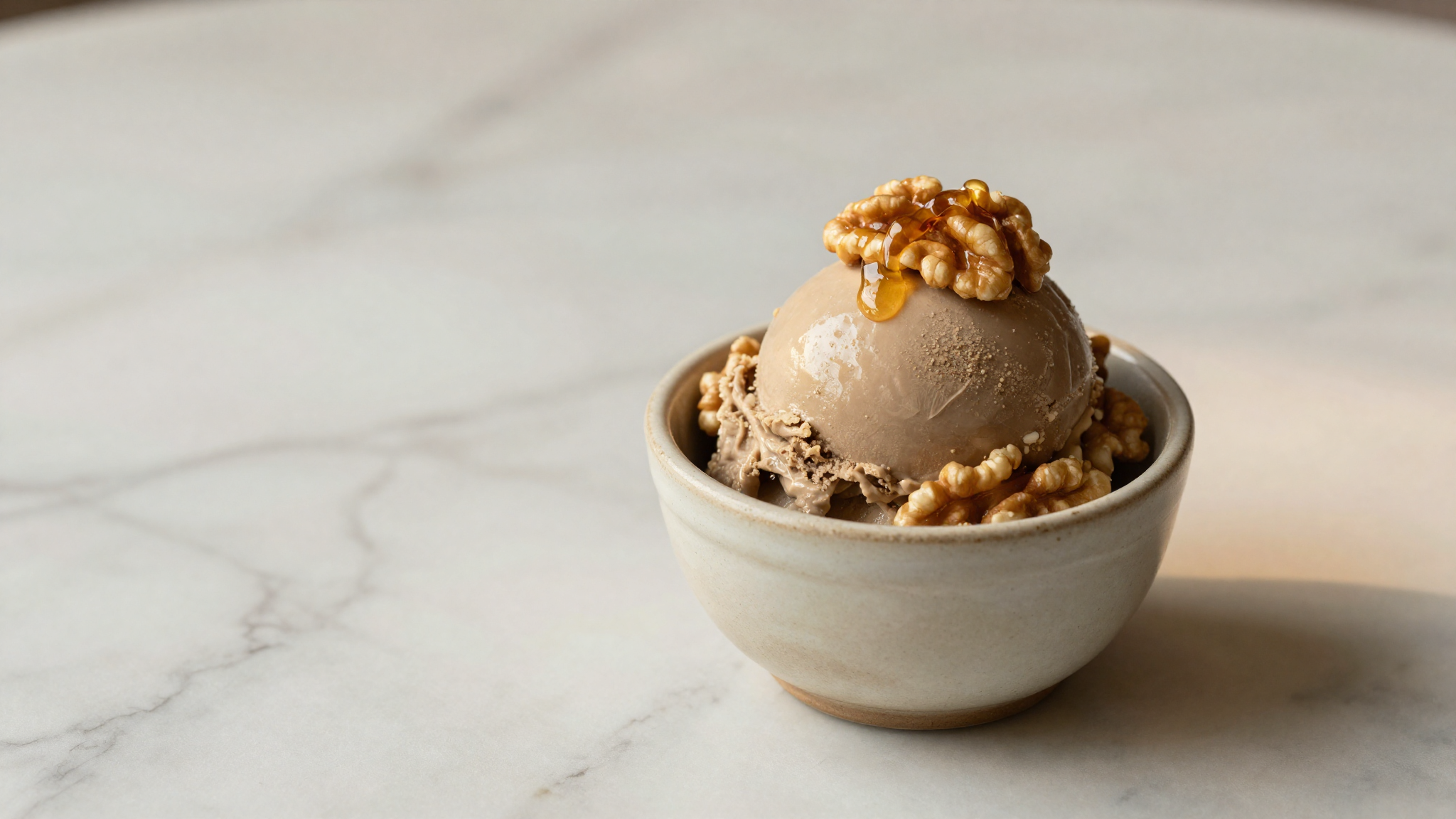 Pale taupe scoop of walnut gelato in a ceramic cup drizzled with honey