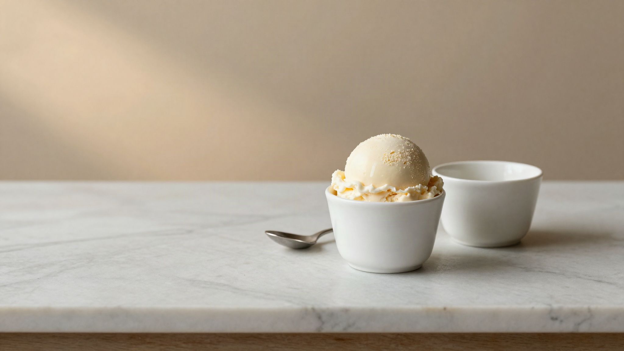 A dense smooth scoop of pale gelato in a small white ceramic cup on marble