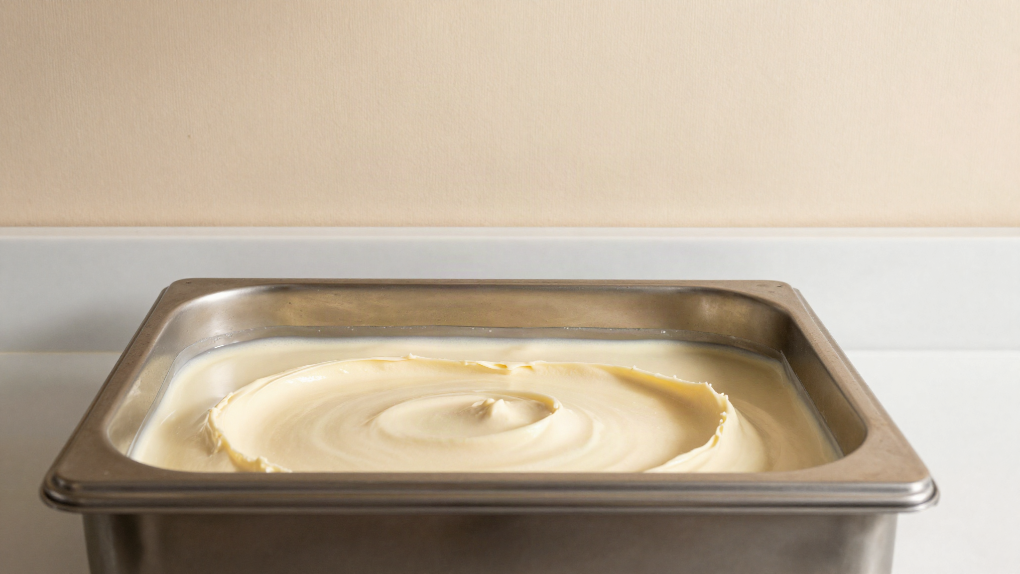 A stainless steel ageing tank of pale gelato mix with a thin clear layer of liquid separated at the surface