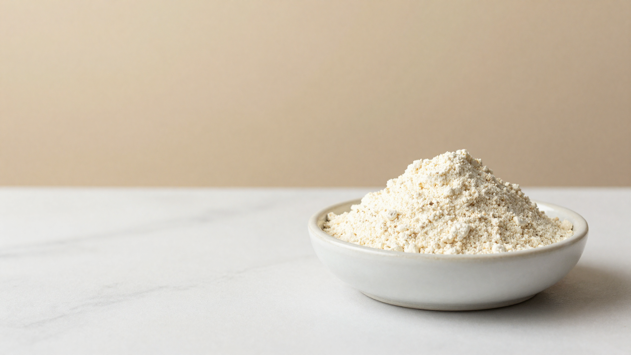 A small ceramic dish of pale ivory whey protein concentrate powder on white marble