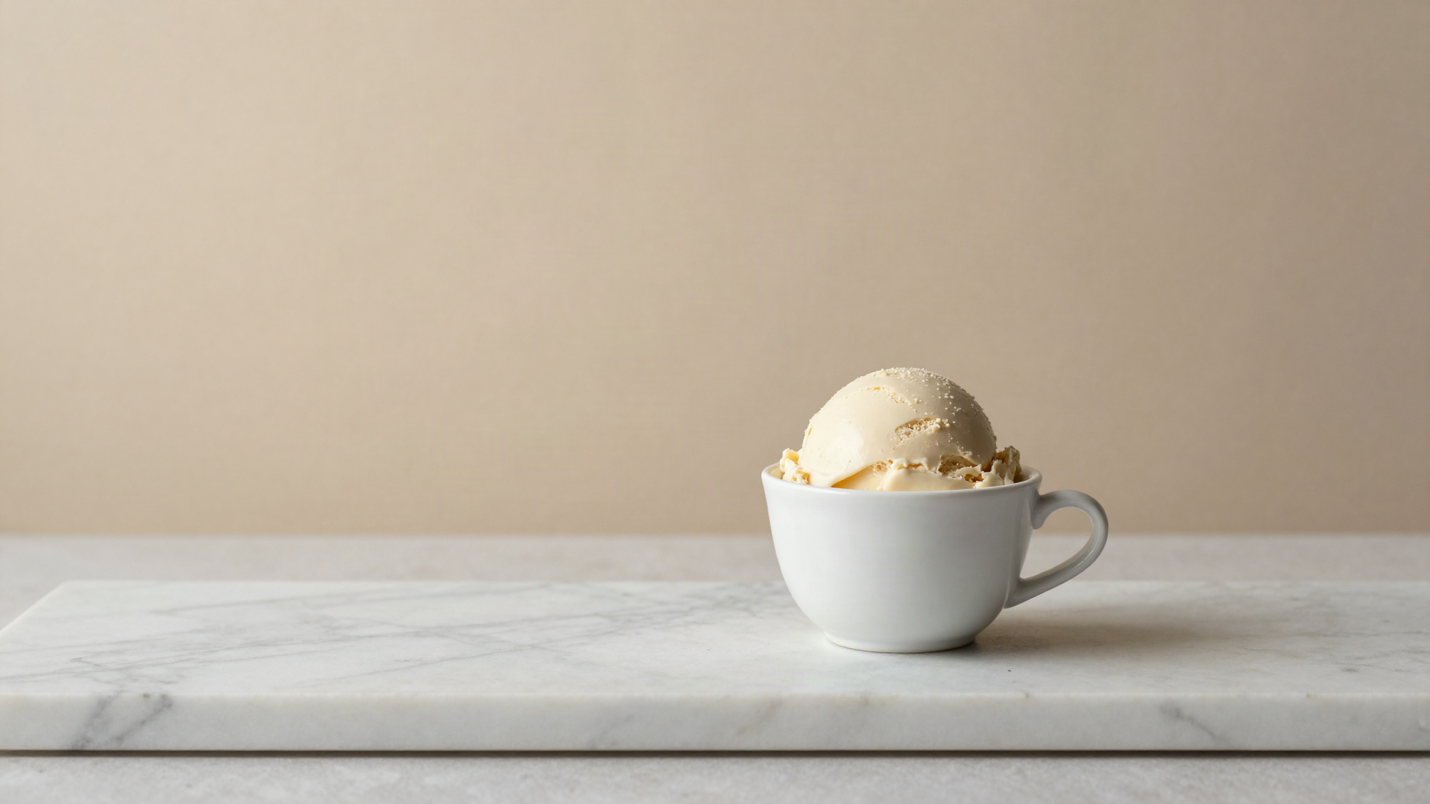 Small white ceramic cup of pale ivory white chocolate gelato on a marble counter