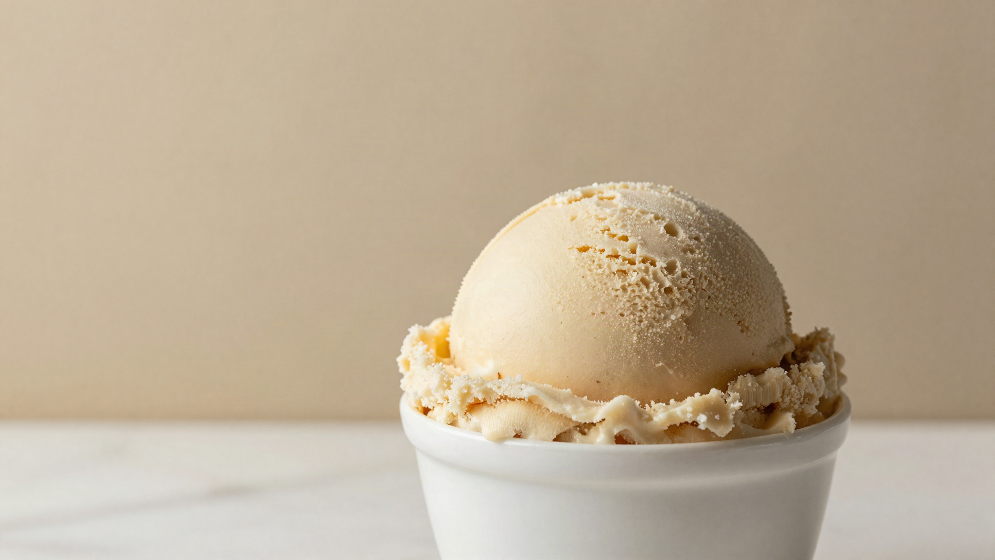 Close-up of a scoop of gelato showing a coarse icy surface in a white ceramic cup on marble