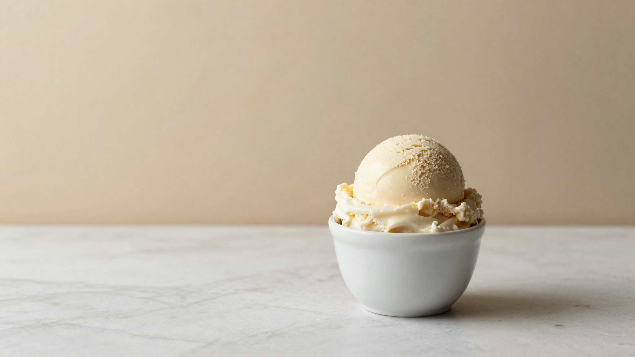 Freshly drawn scoop of italian gelato in a small white ceramic cup on a marble counter