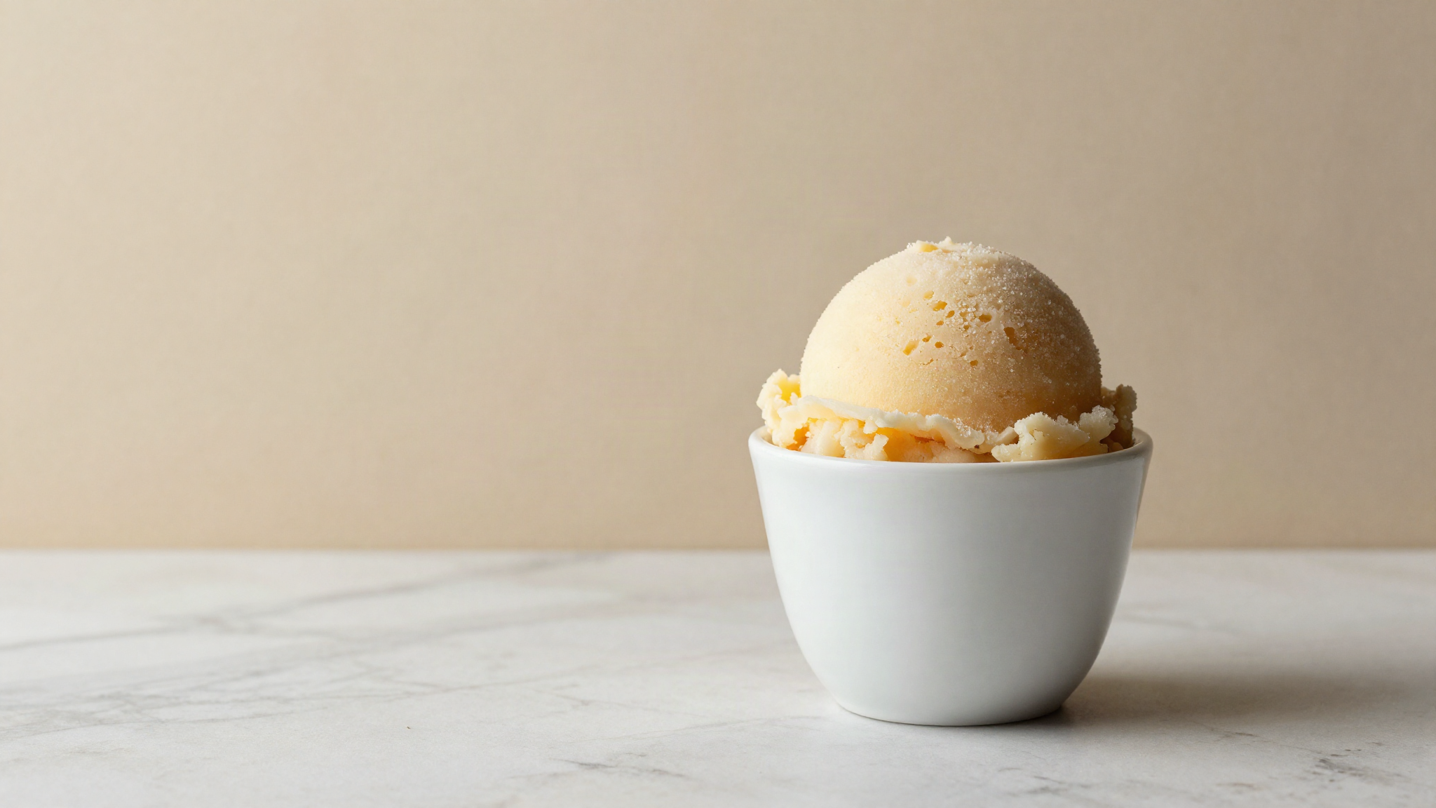 Dense scoop of fruit sorbetto in a white ceramic cup on marble