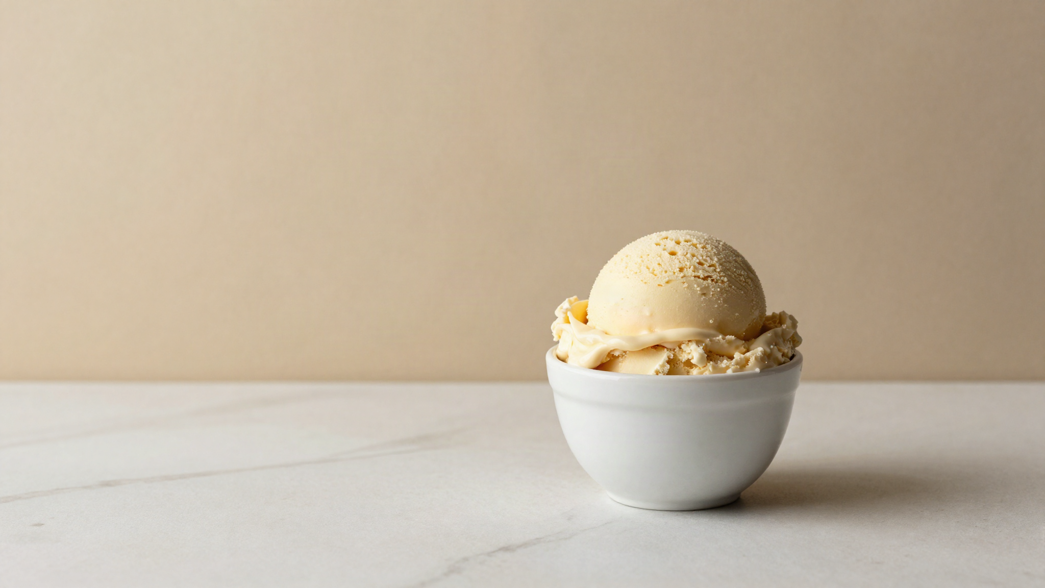A scoop of plant-based gelato holding its shape in a white ceramic cup on marble