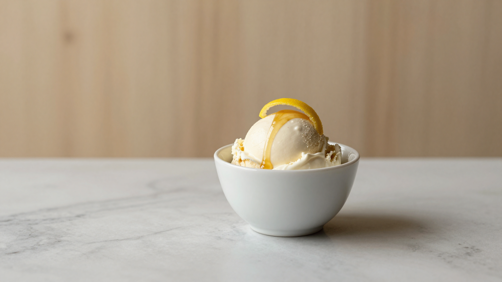 Yogurt gelato scoop with honey drizzle and lemon peel curl in white ceramic cup on marble