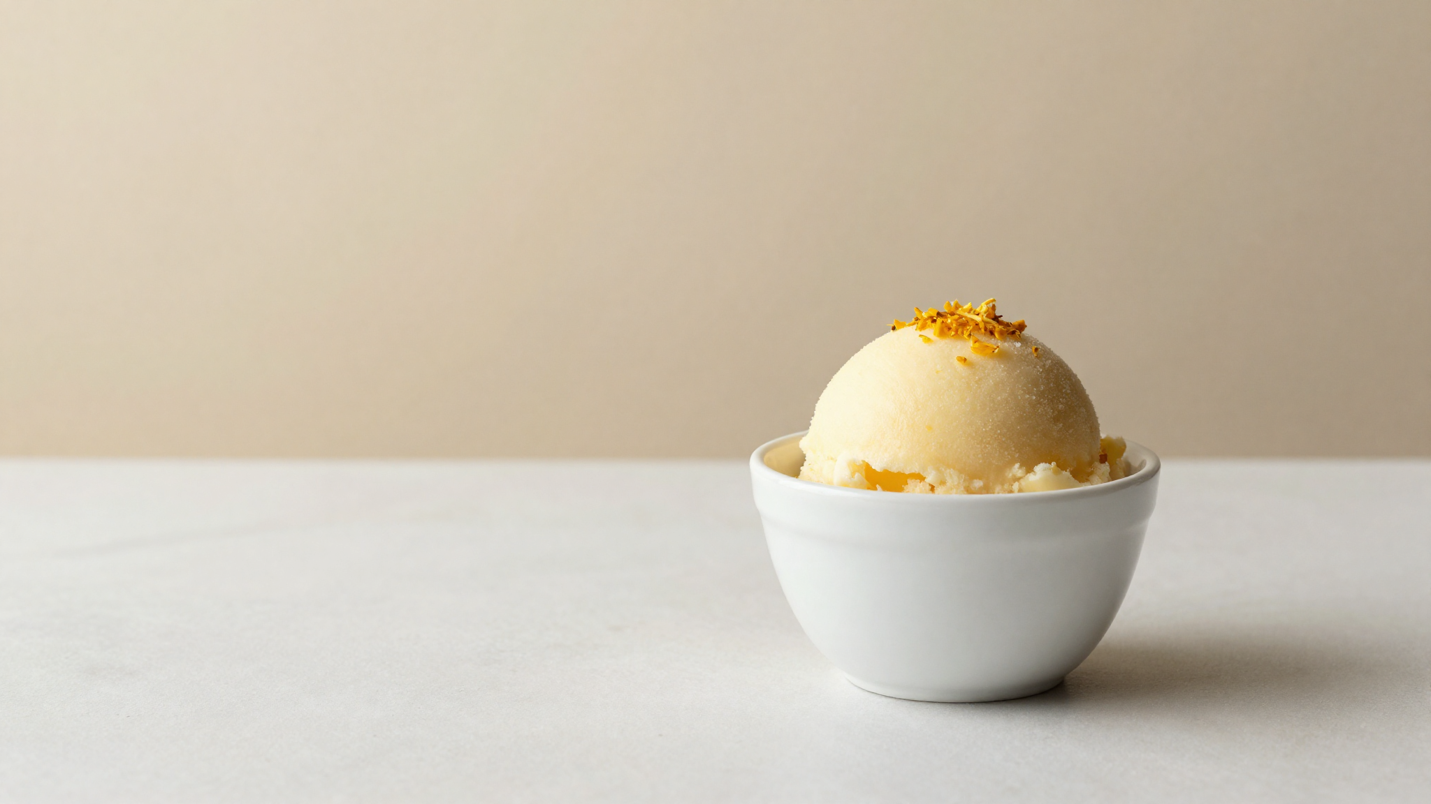 A single elegant scoop of pale yellow yuzu sorbet in a white ceramic cup garnished with fine yuzu zest